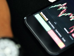 Scalping illustrated by a mobile phone on a trading app and a hand with a wrist watch