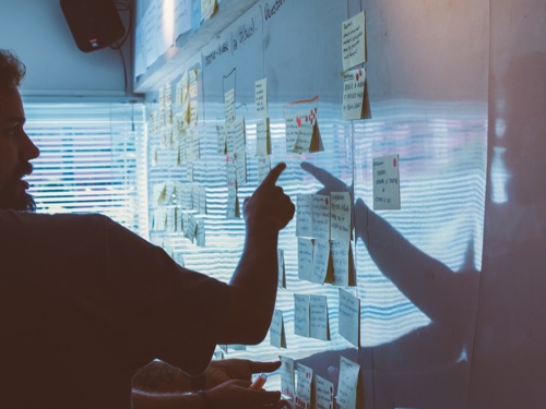 A man pointing to a board filled with post its